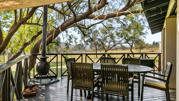 A wooden deck with a table and chairs, a wood stove, and a view of trees and open land. - Peaceful and Private - Luxury Self Catering Home in Lanseria (Lanseria)