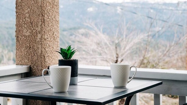 A table with two white textured cups and a small potted plant on a balcony overlooking a mountainous landscape. - Views of Bass Lake, whole house generator, BBQ, Outdoor dining, Mountain Views  (Madera County)