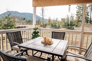 Relax in this serene outdoor seating area with a table and four chairs, overlooking a picturesque landscape with trees and a distant mountain range.