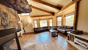 A spacious living room with a stone fireplace, wooden beams, a leather sectional sofa, and a built-in entertainment unit.