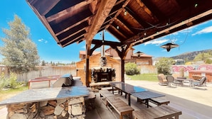 An outdoor patio with stone tables and benches, a wooden pergola, and a stone fireplace.
