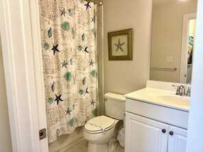 A bathroom with a toilet, a sink, and a shower curtain with a beach theme.