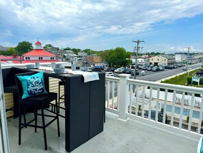 A balcony with outdoor furniture, a view of a street with cars and buildings, and a clear sky.