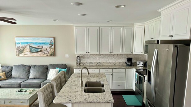 Una cocina moderna con armarios blancos, un refrigerador de acero inoxidable y un rincón comedor con sofá gris y una mesita de centro.