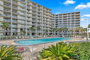 A multi-story hotel with a swimming pool, balconies, and palm trees.