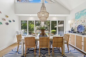 Comedor con candelabro, sillas de mimbre, una mesa dispuesta para cuatro comensales y vistas al verdor exterior.
