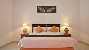Un lit bien fait, recouvert d’une couvre-lit blanche et orange, avec deux lampes assorties de chaque côté, et un tableau au-dessus du lit.