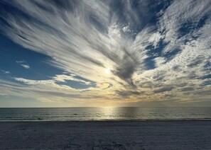 Une plage avec un ciel dégagé et le soleil se couchant ou se levant à l’horizon.