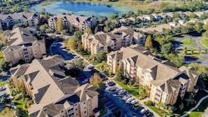 A residential area with apartment buildings, a parking lot, and a lake in the background. - Luxury, Direct Entry Condo 2BR-2BA - Windsor Hills - Only 2 miles to Disney (Kissimmee)