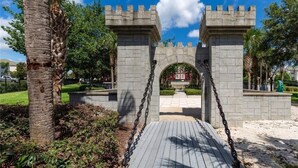 A stone archway with a wooden pathway leading through it, surrounded by greenery and palm trees. - Luxury, Direct Entry Condo 2BR-2BA - Windsor Hills - Only 2 miles to Disney (Kissimmee)