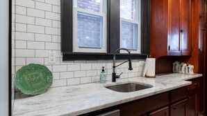 A kitchen with white subway tiles, a black faucet, and wooden cabinets. - Craftsman Charmer | Easy Access to City & Airport (Pittsburgh)