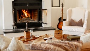 Un salon avec une cheminée, un fauteuil blanc, une guitare et un tapis en fourrure.