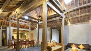 Ein rustikales Interieur mit freiliegenden Holzbalken, einer Essecke mit Tisch und Stühlen sowie einer Sitzecke mit Kissen.