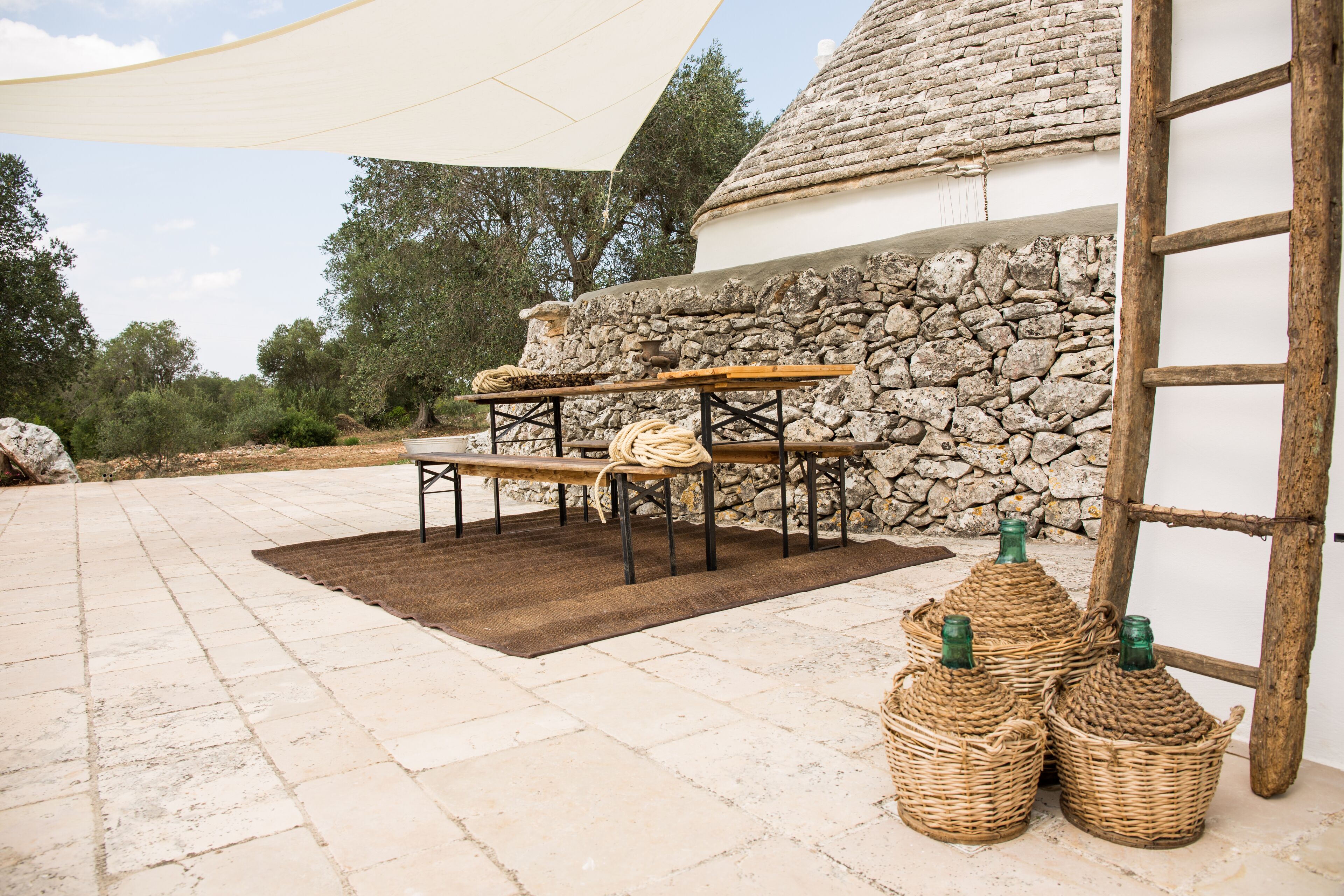 An outdoor patio with a stone table and chairs, surrounded by stone walls and a wooden ladder.