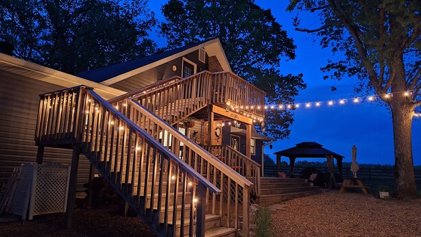 A wooden staircase leading to a deck with string lights, surrounded by trees and a gazebo. - Escape to the Country Penthouse (Dickson)