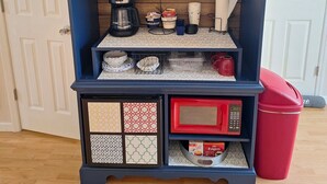 A wooden cabinet with a television mounted above, containing kitchen items like a coffee maker, cups, and a microwave. - Escape to the Country Penthouse (Dickson)