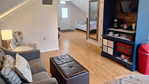 A living room with a sofa, ottoman, and a TV stand with kitchen appliances. - Escape to the Country Penthouse (Dickson)