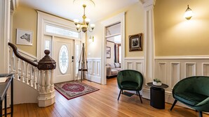 A spacious foyer with a wooden staircase, a chandelier, and green upholstered chairs. - Heritage Location in Heart of Revelstoke (Revelstoke)