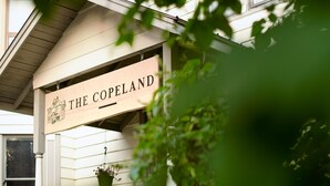 A sign reading "The Copeland" with a house illustration, a hanging flower pot, and a window. - Heritage Location in Heart of Revelstoke (Revelstoke)