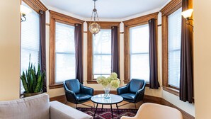 A corner room with two leather chairs, a round table, a vase with flowers, and a large window with curtains. - Heritage Location in Heart of Revelstoke (Revelstoke)