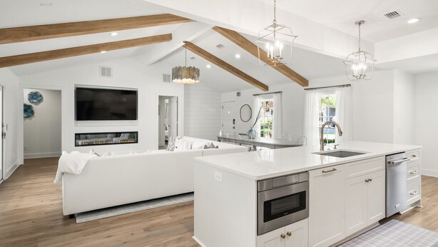 A modern kitchen with white cabinetry, a central island, and a built-in oven. There is a large window with a view of greenery outside.