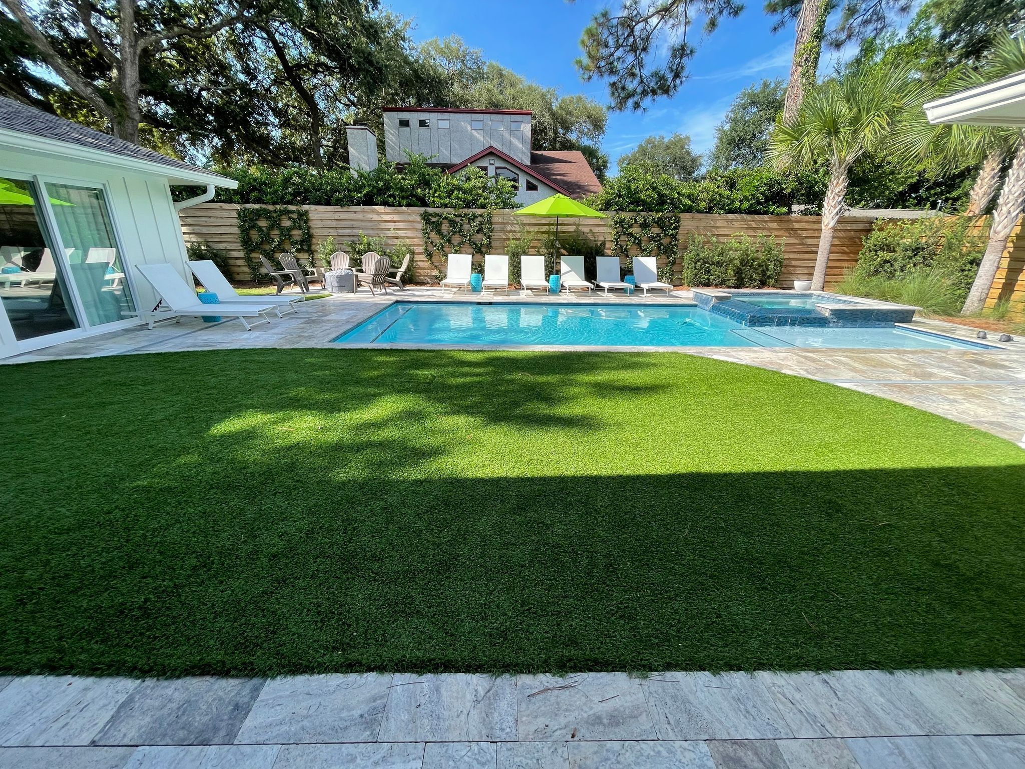 Un jardin avec une piscine, une pelouse artificielle et une clôture en bois.