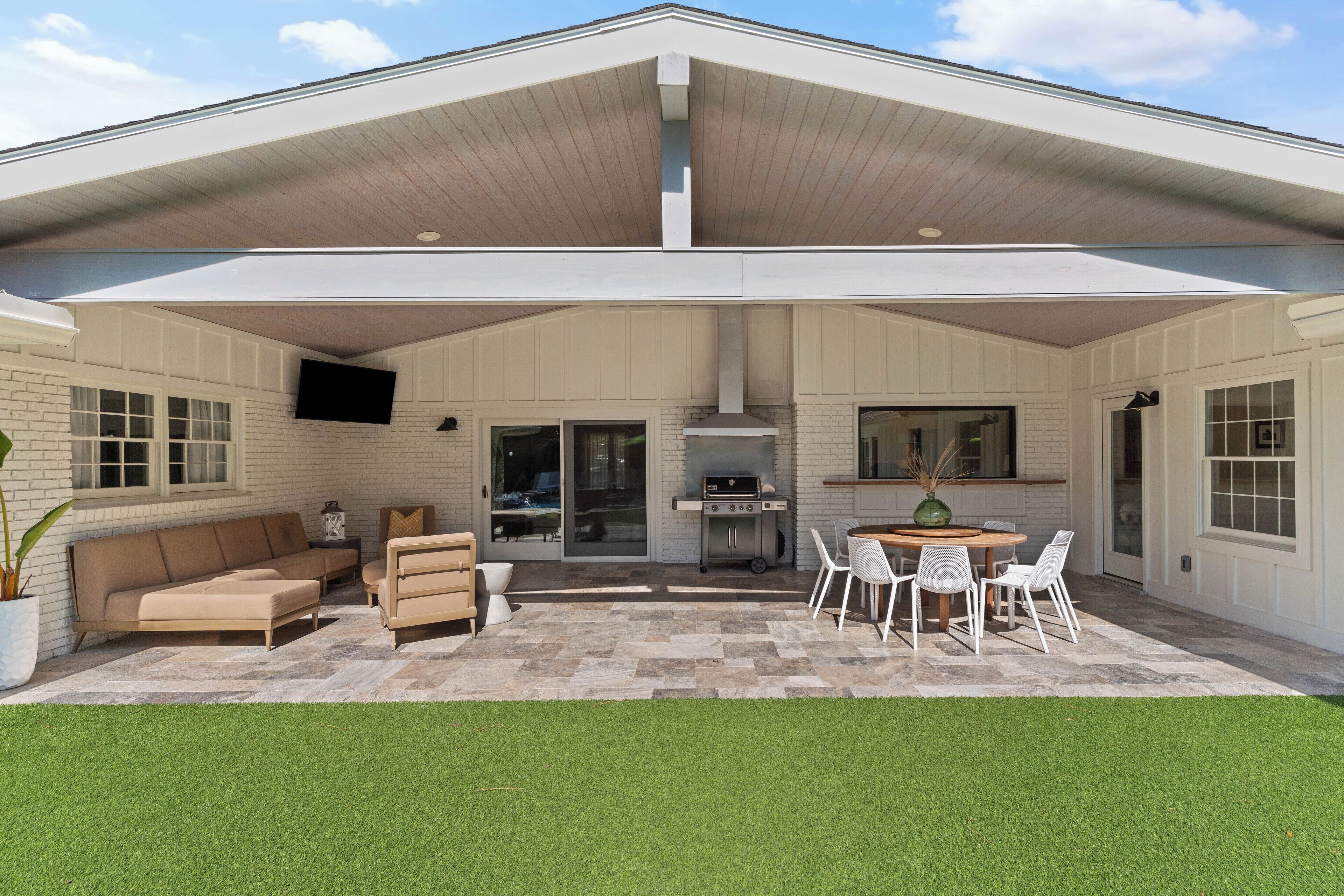 A covered patio area with a barbecue grill, seating, and a view of the house.