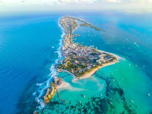 An aerial view of a coastal town with a long shoreline, a central pier, and numerous boats in the water.
