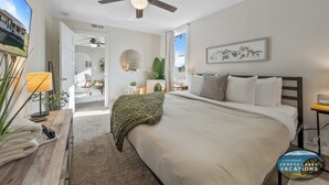 Un dormitorio con una cama grande, un ventilador de techo, una ventana con vistas y un cuadro en la pared.