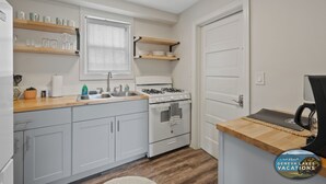 Una cocina compacta con armarios blancos, una estufa, un fregadero y estanterías de madera.