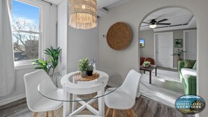 Un salón moderno con una mesa de vidrio, sillas blancas, un tapiz tejido y vistas al exterior.