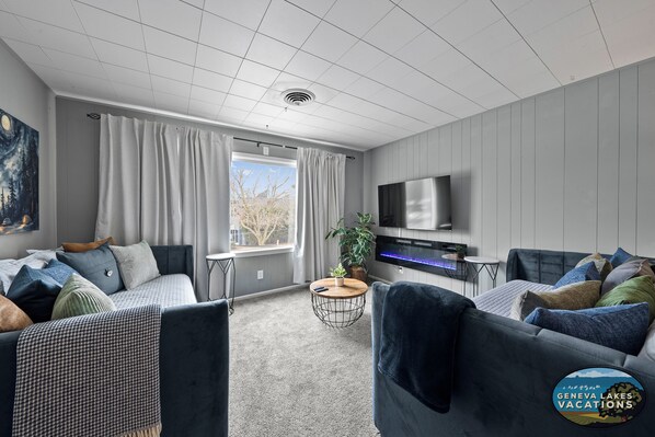 Un salon moderne avec un canapé gris, une table basse ronde et un téléviseur fixé au mur.