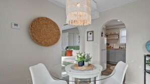 Un espace repas moderne avec une table en verre et des chaises blanches, une décoration murale tissée et un luminaire suspendu.