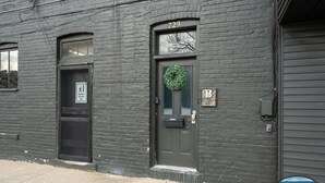 Un immeuble à la façade en briques sombres, portant le numéro 729, avec une porte ornée d’une guirlande et une boîte aux lettres.