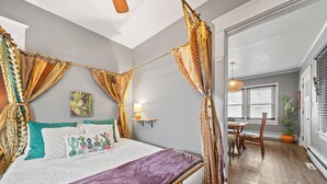 Une chambre à coucher avec un lit, des rideaux, une table de chevet, une lampe et une fenêtre.