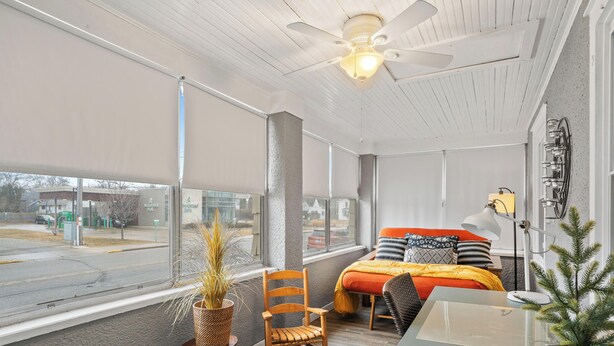 Une pièce comprenant un lit, un bureau, une chaise, un ventilateur de plafond et une grande fenêtre.