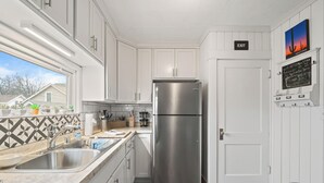 Une cuisine moderne avec des meubles blancs, un réfrigérateur en acier inoxydable, un évier et une fenêtre donnant sur des maisons.
