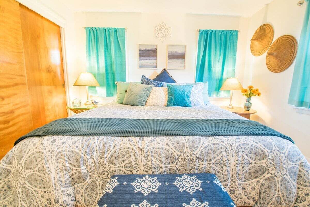 A bedroom with a bed, two nightstands, a window with curtains, and a wall with decorative items.