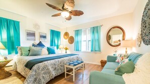 Un dormitorio con cama, sillón, sofá, ventilador de techo y ventana con cortinas.