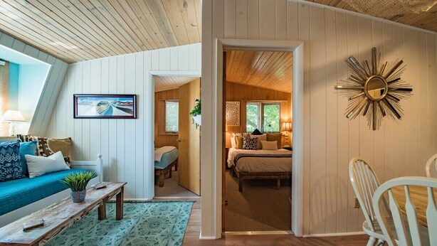 Ein gemütlicher, gut beleuchteter Raum mit Holzbalkendecke, einem Bett mit Kopfteil, einem Nachttisch und einem Wandspiegel.
