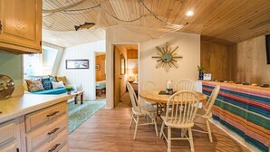 Ein gemütliches Zimmer mit Holzbalkendecke, einem runden Esstisch mit Stühlen, einer farbenfrohen Sitzbank mit Streifenmuster und einem dekorativen Wandspiegel.