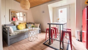 A cozy room with a wooden ceiling, a sofa with cushions, a small round table, red chairs, and a red refrigerator. - Geneva Beach House Como Suite Walk to Lake Shore Path Near Downtown (Lake Geneva)