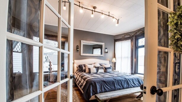 Un dormitorio con cama, un banco, un espejo y una ventana.