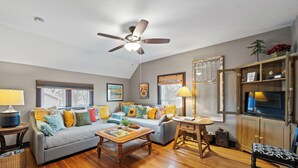 A cozy living room with a ceiling fan, a sofa set, a coffee table, and a bookshelf.