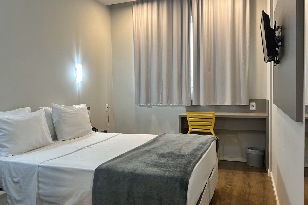 A hotel room with a bed, a desk, a chair, and a window with curtains.