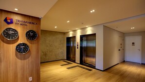 Hall del hotel Transamerica Fit con cuatro relojes, dos ascensores y suelo de madera.