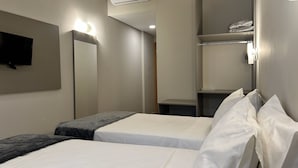 Habitación de hotel con dos camas, un televisor montado en la pared y un estante con toallas dobladas.