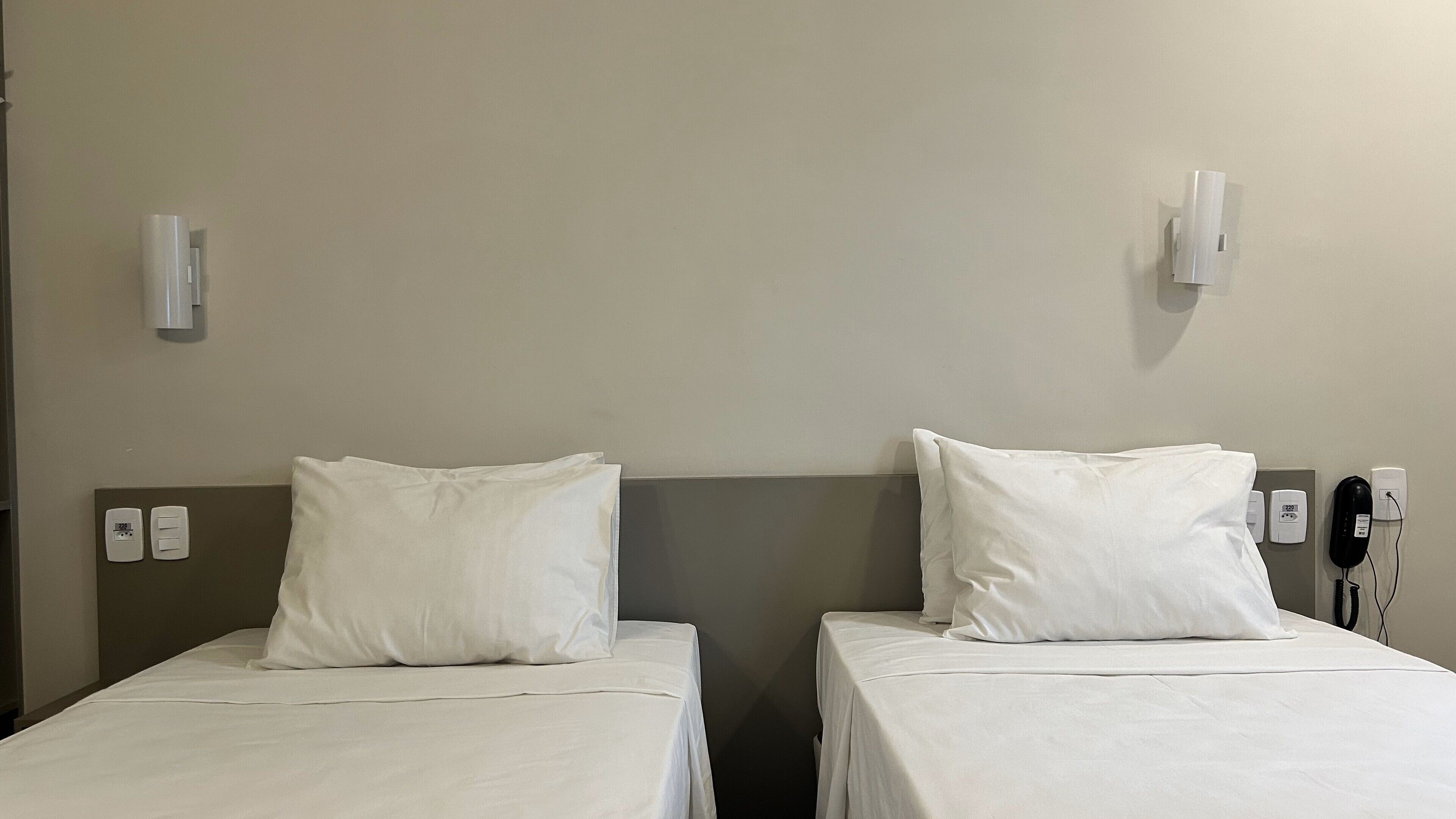 Duas camas de solteiro com lençóis brancos em um quarto de hotel.