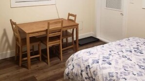 A room with a wooden desk, a bed with a floral bedspread, a mounted TV, and a door with a window. - Bachelor's Green Oasis: With Putting Green (Langford)