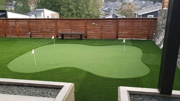 A backyard with artificial green turf, a wooden fence, and a stone bench. - Bachelor's Green Oasis: With Putting Green (Langford)